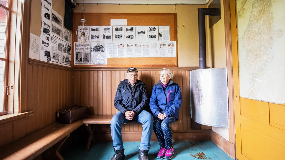 Ylva Rudin och Ingvar Jakobsson i 3:e klassens väntsal i Tjuls stationshus. Väggfärg och inredning är helt i original. Under kalla vinterdagar kunde besökarna värma sig vid kaminen som syns till höger.