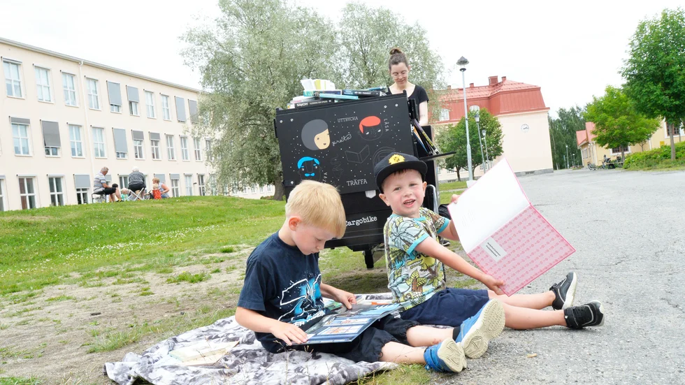 Wille och Hampus Eriksson slår sig ner i gräset och bläddrar i böckerna. 
