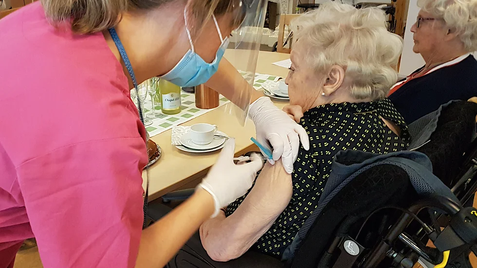 Sjuksköterskan Ann-Louise Broberg ger Gun-Britt Johansson andra dosen av covid-vaccin. Därefter kaffe och bubbel. 