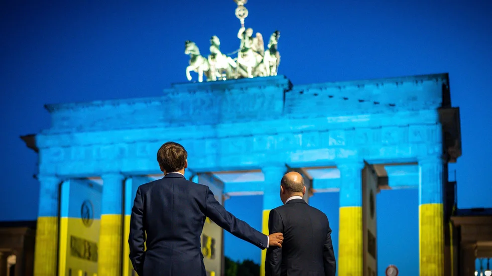 Frankrikes president Emmanuel Macron och Tysklands förbundskansler Olaf Scholz vid Brandenburger Tor, upplyst i ukrainska färger, efter ett möte i Berlin i maj. Arkivbild.