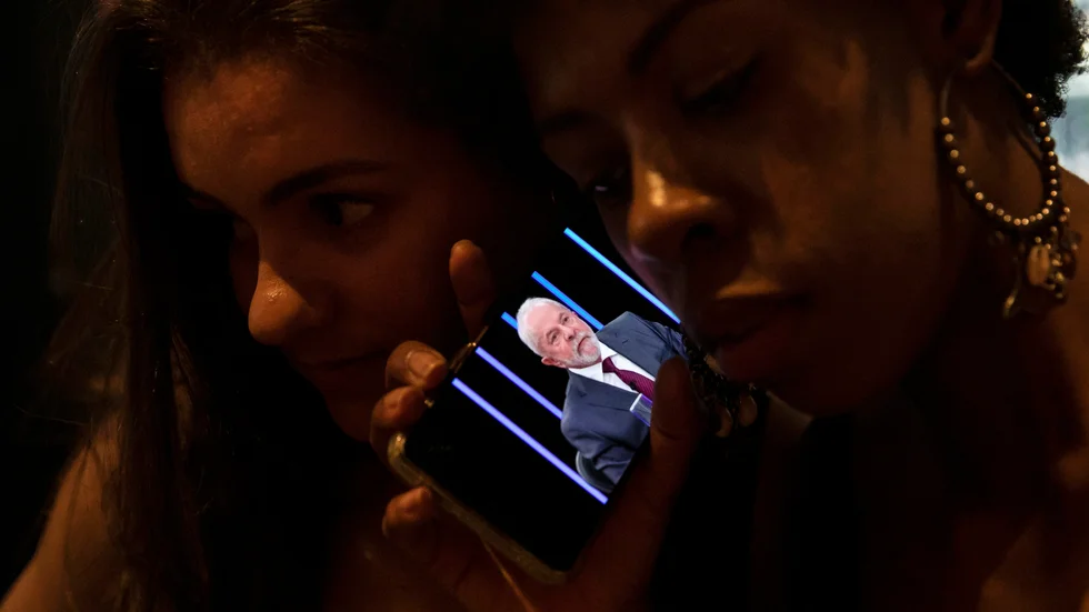 Några kvinnor i Rio de Janeiro lyssnar och tittar i en mobiltelefon när Lula da Silva intervjuas i Jornal Nacional.