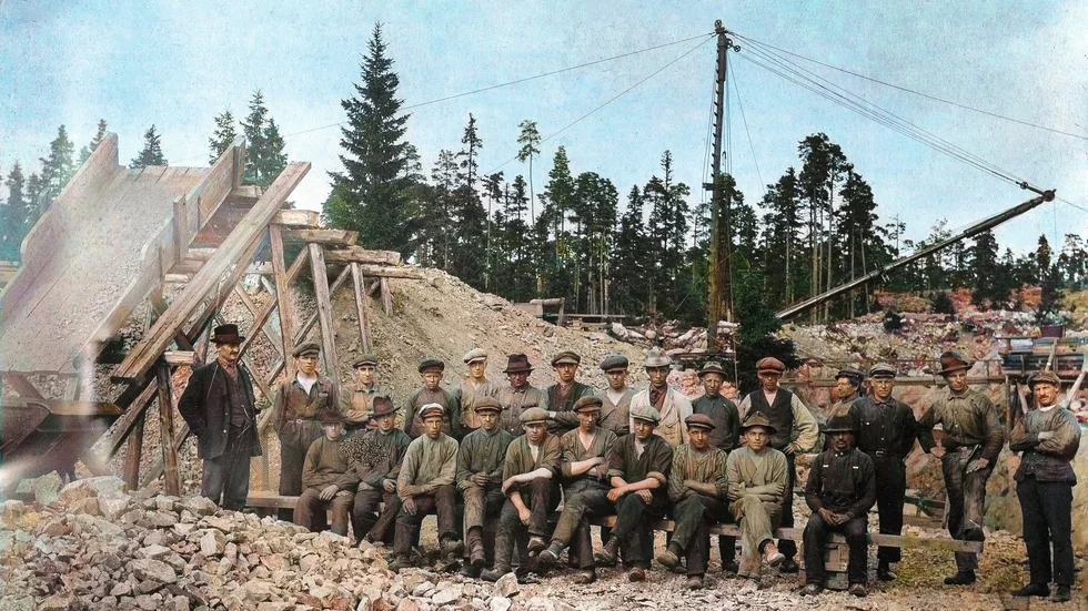Ett arbetslag i gruvan på Kallaxön i augusti 1922. Till vänster ses sorteringsverket och till höger uppfordringsverket med lyftkran.