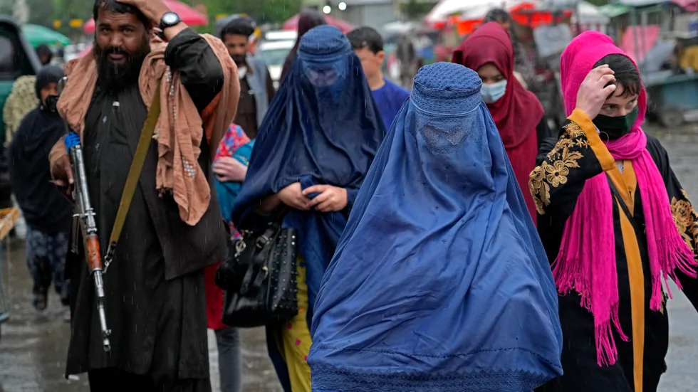 Afghanska kvinnor flankerade av beväpnade talibaner på en marknad i Kabul i maj.