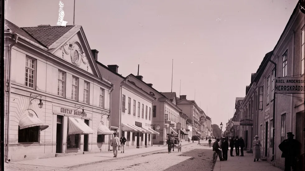 Västra Storgatan i Nyköping, omkring år 1900. Vänster sida: Gustav Larssons järnhandel. Höger sida: Axel Anderssons herrskrädderi, Hedvig Sandbergs mode och tapisseriaffär.