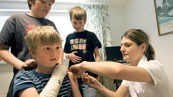 Linus Åbrink får vaccinspruta av Kristiina Kask medan Oliver och Albin Åbrink tittar på.
