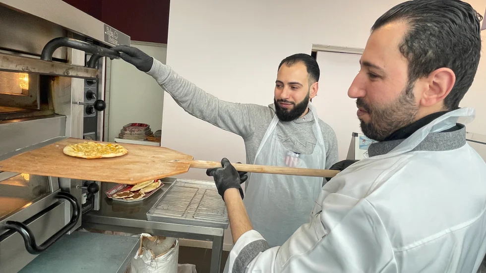 Mahmoud Deeb tar ut en nygräddad syrisk pirog ur ugnen på Piroghuset i Gottsunda, medan hans bror Abdullah assisterar.