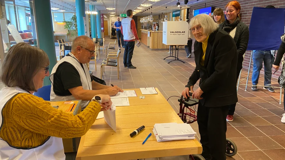 Röstmottagarna Evy Söderberg och Brage Öberg tar emot Elin Fredrikssons tre kuverten. "Det känns bra att ha röstat", säger Elin som är jämngammal med den kvinnliga rösträtten.