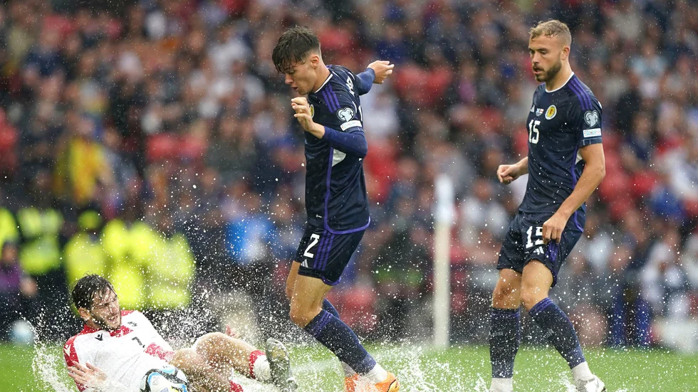 Skottlands Aaron Hickey, i mitten och Georgiens Khvitja Kvaratschelia kämpar om bollen i blötan på Hampden Park.