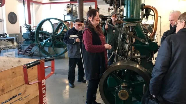 Guiden Giselle omgiven av SRF medlemmar framför en av maskinerna i turbinhallen.