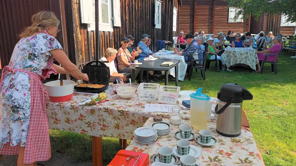 Margareta Erstam vid våffeljärnet och besökare som njöt i solen.