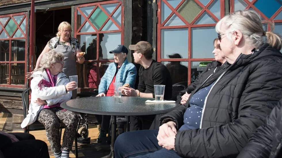 Fia Wilensjö serverar och i solen sitter, från vänster: Inger Larsson, Sven Andersson, Erik Ström, aktivitetsledare, Maj-Britt Söderlind och Christina Andersson.