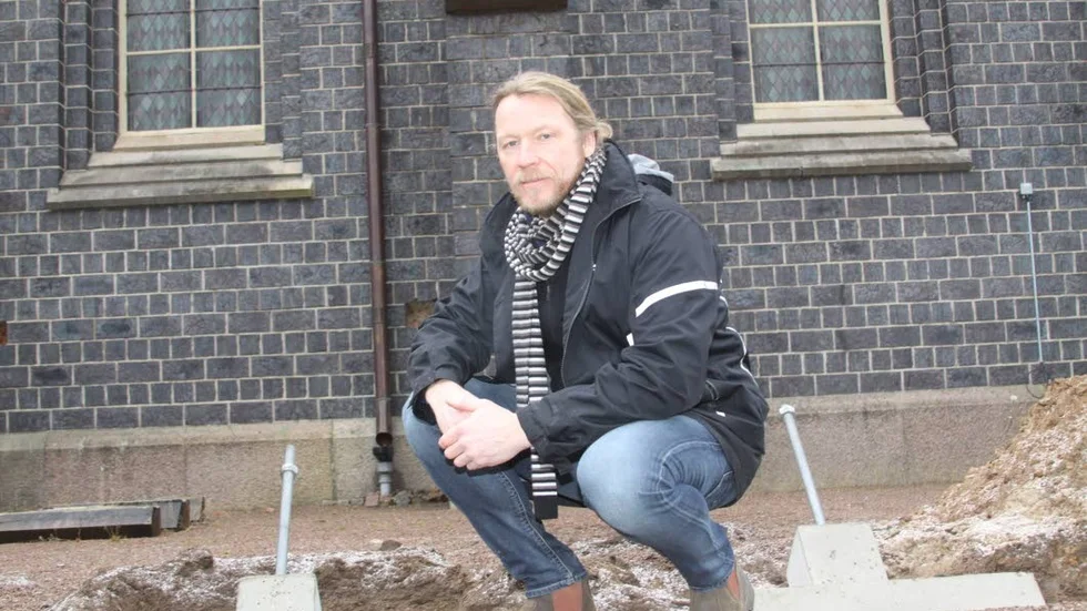 Boxholms kyrka. Fredrik Åstrand, sitter på huk mellan två plintar och med en strävpelare bakom huvudet. Plintarna är förberedelse för att sätta upp stämp.