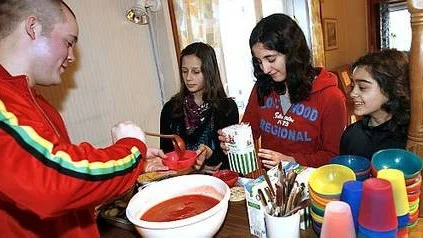 Fritidsledaren Martin Lindgren serverar mellanmål till Layla Noroozy, Hanna Neichalani och Perna Jalili.