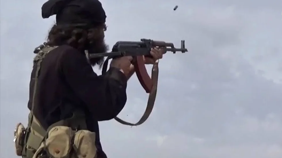 En skärmdump från ett videoklipp publicerat av Islamiska statens kommuniktionsorgan föreställande en IS-krigare som avfyrar sitt vapen mot syriska trupper.
