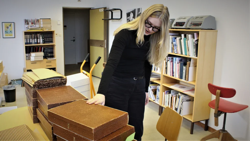 Miranda Cox går igenom maskinskrivna dokument i bruna arkivmappar från Facit. Forskarrummet på Brukskultur bär andra tidsdokument, som räknemaskiner och kontorsmöbler från olika tider.