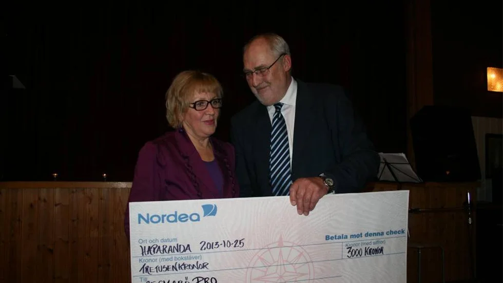 Kommunalrådet Gunnel Simu överlämnar en check på 3000 kr i jubileumsgåva från kommunen, som tas emot av ordföranden Roland Harr.