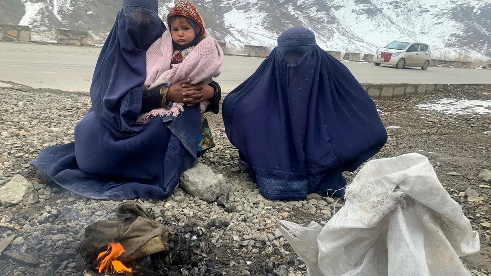 Två kvinnor och en 1,5 år gammal pojke värmer sig vid en brasa i östra Afghanistan i januari 2022.