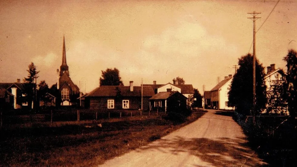 Vy från 30-talet. Norrfjärdenvy från 1930-talet. Till vänster ses Tjärnqvists smedja och Sandbergs bageri. I bakgrunden den kyrka som totalförstördes vid brand 1963.
