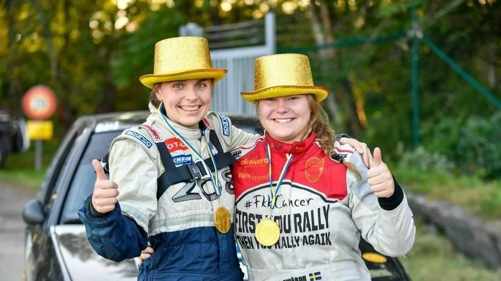 Madicken Swärdh, till höger, tillsammans med kartläsaren Viktoria Johansson i sina guldhattar och medaljer efter målgången vid den sista SM-tävlingen i Trollhättan. Den riktiga guldmedaljen får hon hämta ut i samband med en stor nationell bilsportgala i början av nästa år. Men svensk mästare kan hon titulera sig med sedan i lördags eftermiddag.