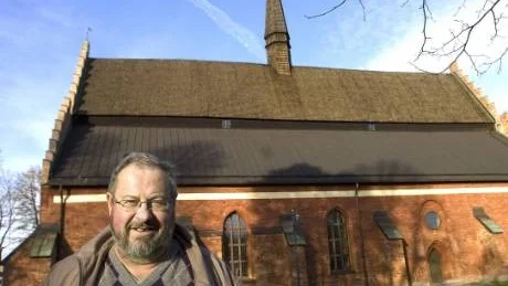 Svenska kyrkans fastighetsskötare Pelle Holm framför S:t Laurentii kyrka. Det är denna södra sida av spåntaket som måste bytas. Kostnad: 1 miljon.