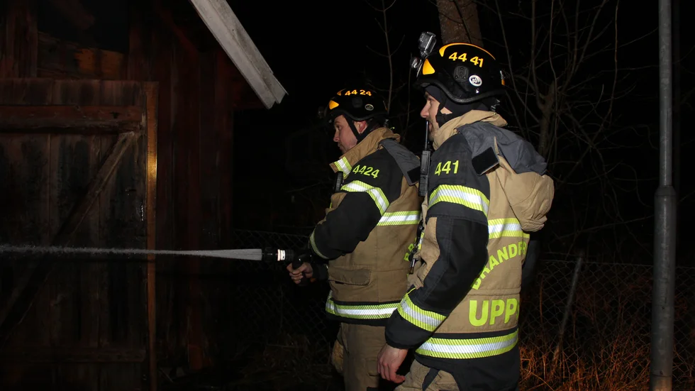 Mikael Lind och Robin Björn, deltidsbrandmän från Gimo brandkår sprutar vatten i uthuset för att stoppa spridning av branden. De hade varit på plats ända sedan klockan 13.30 i det kyliga vädret.