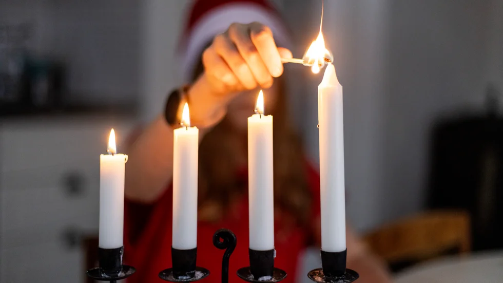 En flicka i tomteluva tänder det fjärde ljuset i advent.