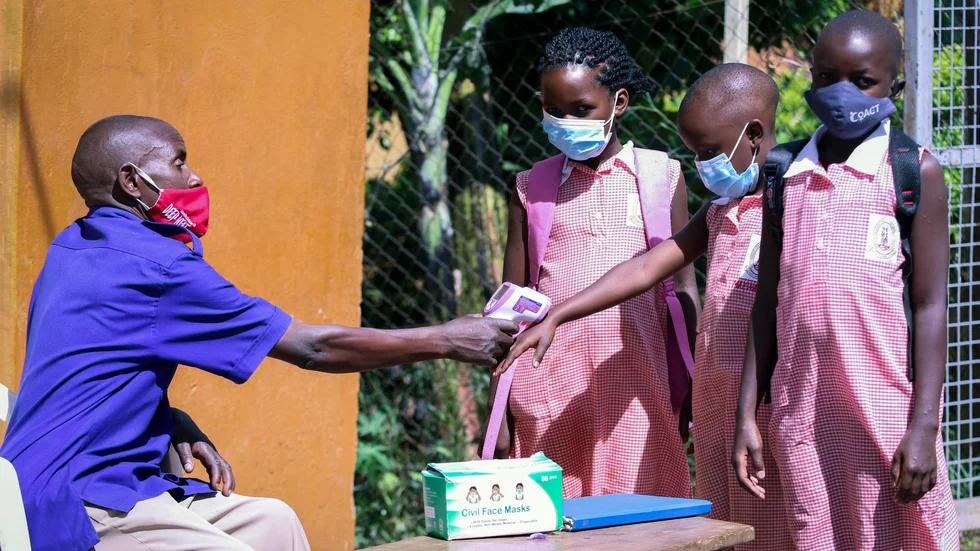 En skolvakt kontrollerar temperaturen på återvändande skolbarn i Uganda.