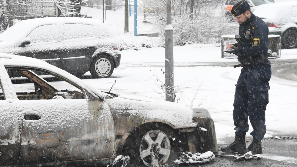 En polisman vid en utbränd bil på en parkering i förorten Rinkeby utanför Stockholm efter upplopp den 20 februari. Oroligheterna började i samband med att polisen skulle göra ett ingripande och frihetsberöva en person. Foto: Fredrik Sandberg/TT Foto: Fredrik Sandberg/TT.