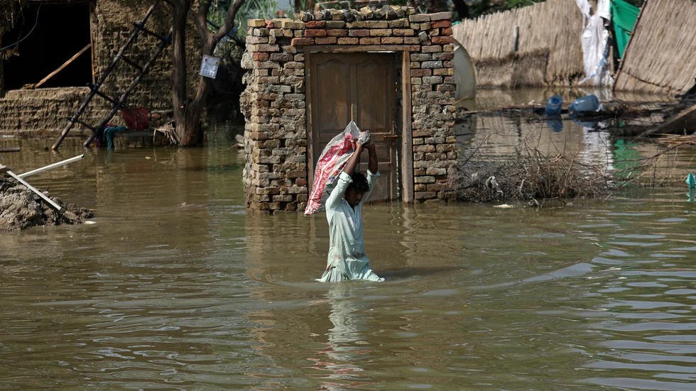 En man bär tillhörigheter från sitt översvämmade hem i Pakistan. FN:s väderorganisation WMO bedömer att väderfenomenet La Niña kommer att fortsätta i ett halvår till.