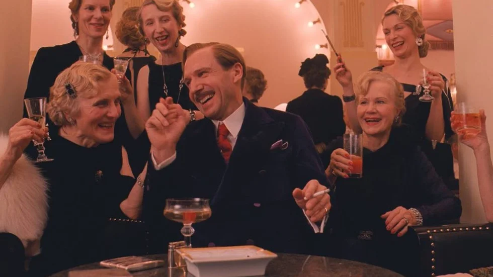 Tjusare. Ralph Fiennes spelar huvudrollen, den charmerande consiergen Gustave, som har ett mycket gott öga till The grand Budapest hotels äldre kvinnliga klientel.