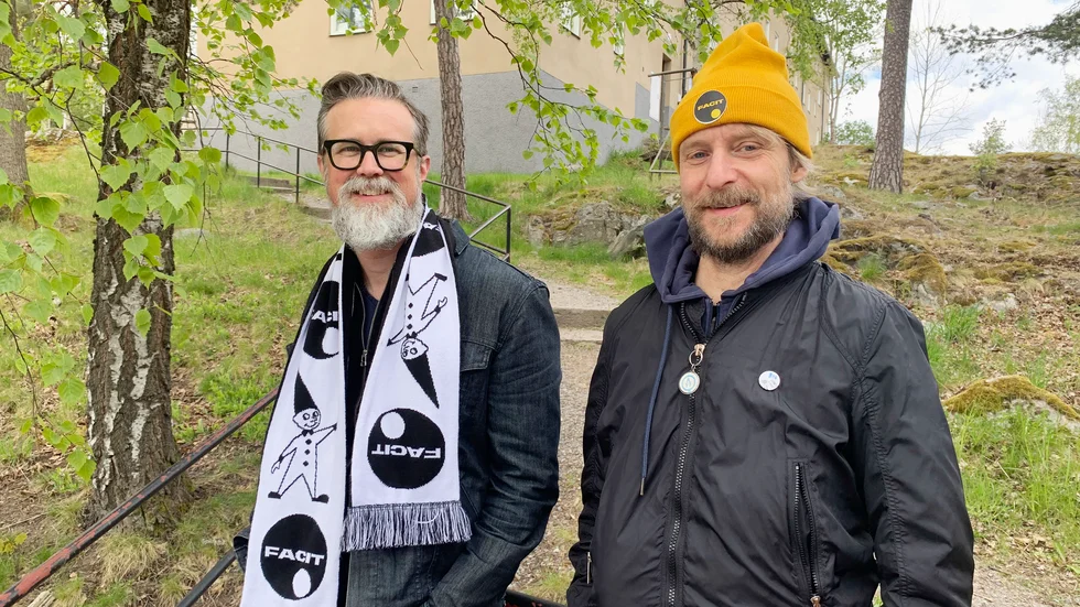 Det kylslagna majvädret kräver halsduk och mössa, självklart med Facit-logga. Författarna till Folket på Facit, Daniel Carlberg och Christer Engström visar en rad andra Facitsouvenirer i boken som släpps i slutet av månaden.