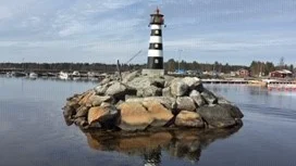 Havet ligger spegelblankt vid den gamla fyren i Kallax fiskehamn.