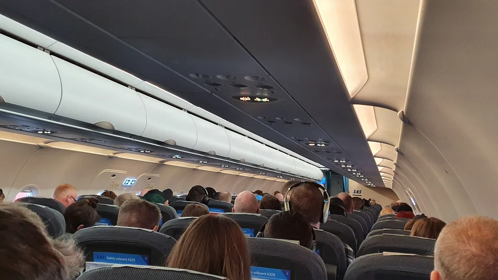 I avgångshallen och  i säkerhetskontrollen uppmanas resenärerna att hålla avstånd. Men väl ombord sitter passagerarna som packade sillar.