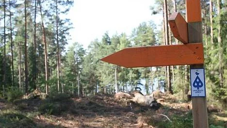 Upplandsleden typiska orange vägvisare har hamnat mitt i ett hygge för den nya genomfartsleden i Bredsand utanför Enköping. I bakgrunden lyser Svinnegarnsviken blå.