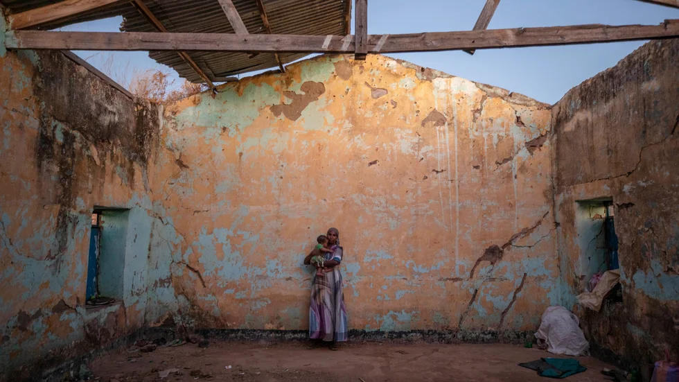 En tigreansk kvinna och hennes barn står i ett hus som tjänstgör som en tillfällig flyktingbostad på andra sidan gränsen i Sudan.