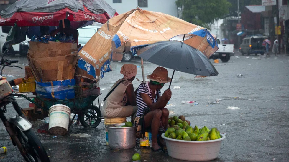 Gatuförsäljare kurar under den tropiska stormen Laura i Port-au-Prince i Haiti på söndagen.