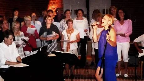 Sångsolisten Hanna Lindblad framför den tillfälligt framlockade Kören i Östra Eds kyrka på onsdagskvällen.  Till vänster vid pianot programledaren Erik Gruvebäck.