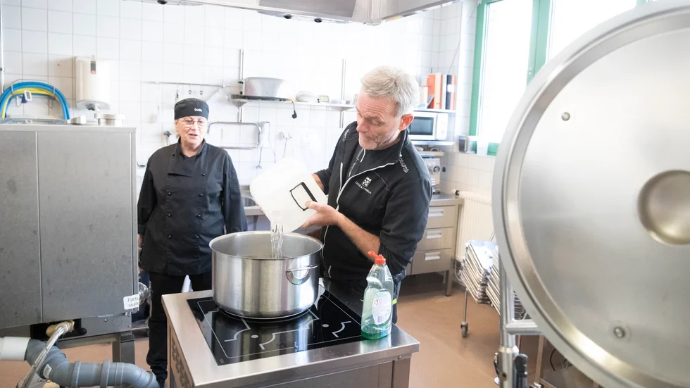 Vaktmästaren Roger Lindberg hjälper kokerskan Gunilla Sundström att hälla i vatten i grytan. Det varma vattnet ska sedan användas till att torka borden i matsalen. 