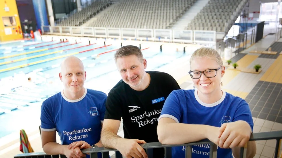 Christoffer Andersson, Christian Brand och Lina Rosvall är redo att välkomna många av landets främsta simtalanger till Munktellbadet. I bakgrunden syns den tillfälliga läktaren som ska hjälpa till att skapa extra bra stämning i Sum-Sim.