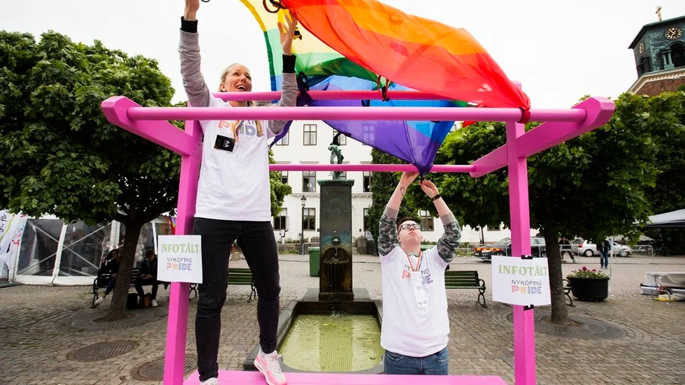 Volontärerna Rasmus Lindh och Josefin Juvelius kämpar för att få styr på Prideflaggan i blåsten.