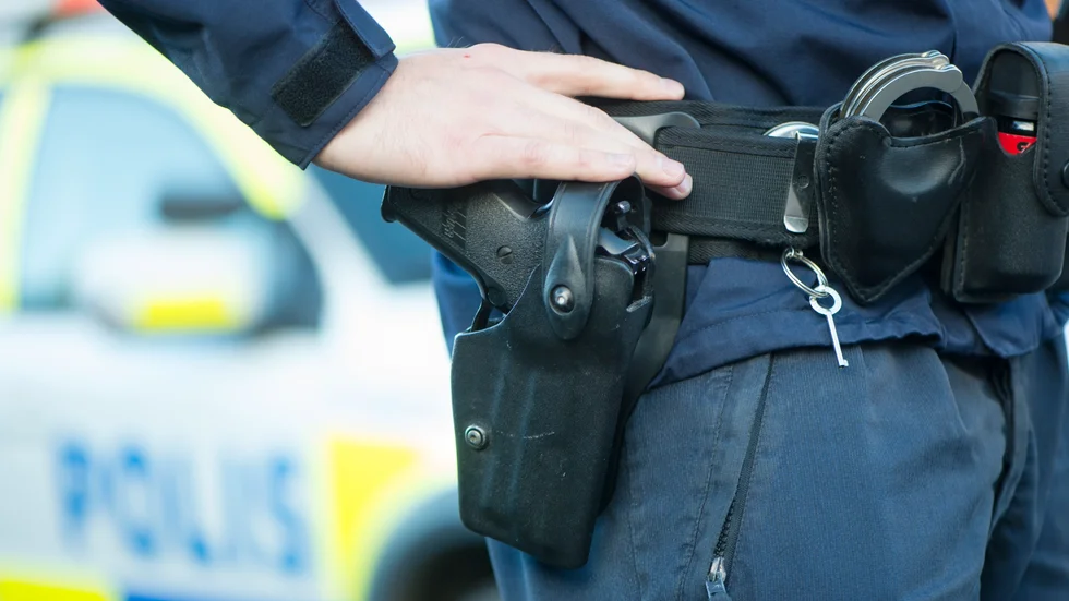 En polis med sitt vapen, en Sig Sauer, i hölster. I bältet syns också ett par handfängsel och pepparsprej.