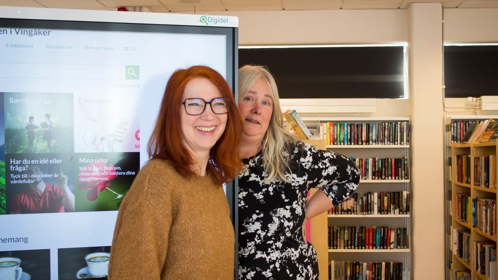 Ulla Solsmo, bibliotekschef, och Christina Strender, socialbibliotekarie på Vingåkers bibliotek, står framför den digitala skärm där deras nya hemsida visas. 