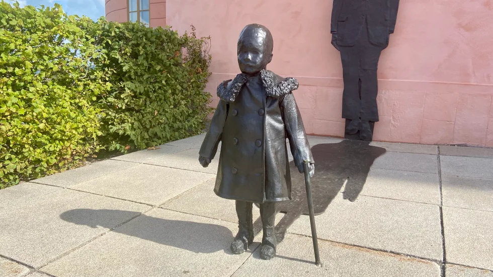 Ett gammalt fotografi av Dag Hammarskjöld som lekande pojke på borggården inspirerade Charlotte Gyllenhammar till den främre delen av konstverket. Nu är det förvanskat i och med att staven brutits av på mitten.
