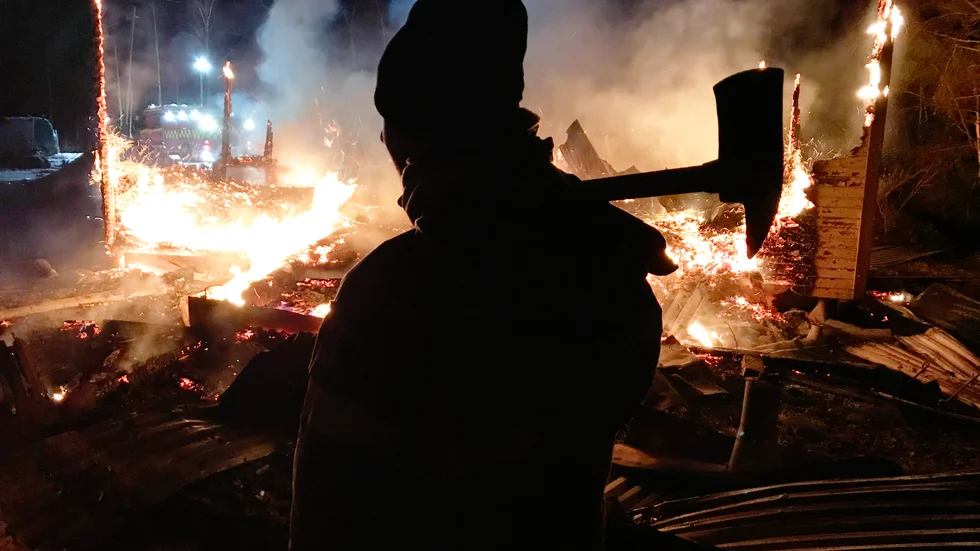 En mindre stuga i Hertsölandet är helt nedbrunnen. En brandman bevakar elden.