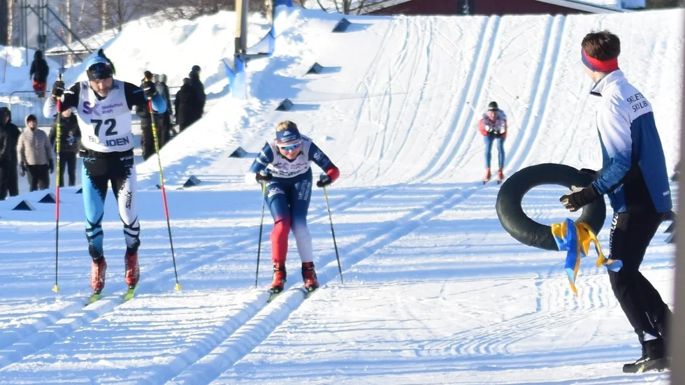 Ella Burman spurtar mot mål i sällskap med Ola Backman, Skellefteå XC. Tore Tiburzi, som själv vann öppna klassen över 22 km, står redo med segerkransen.
