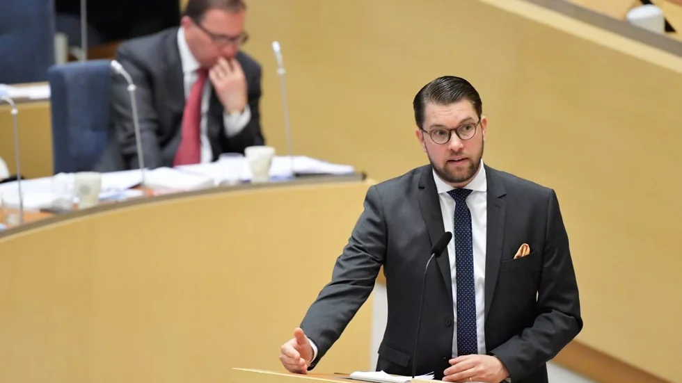 Jimmie Åkesson (SD) i talarstolen under riksdagens partiledardebatt. Statsminister Stefan Löfven (S) i bakgrunden.