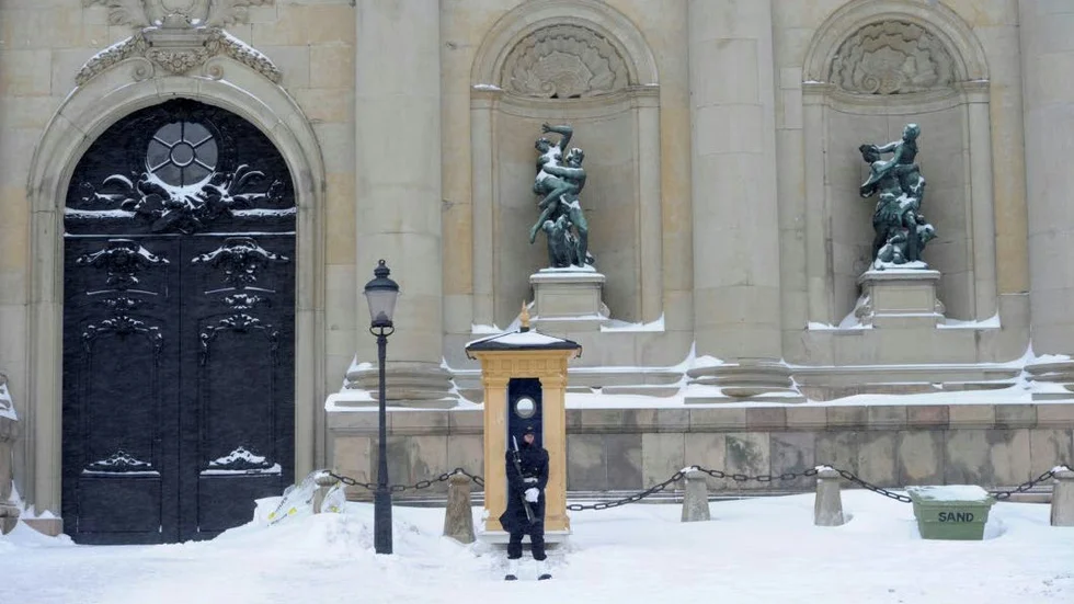 Påpälsad högvakt patrullerar Stockholms slott i snöfall.