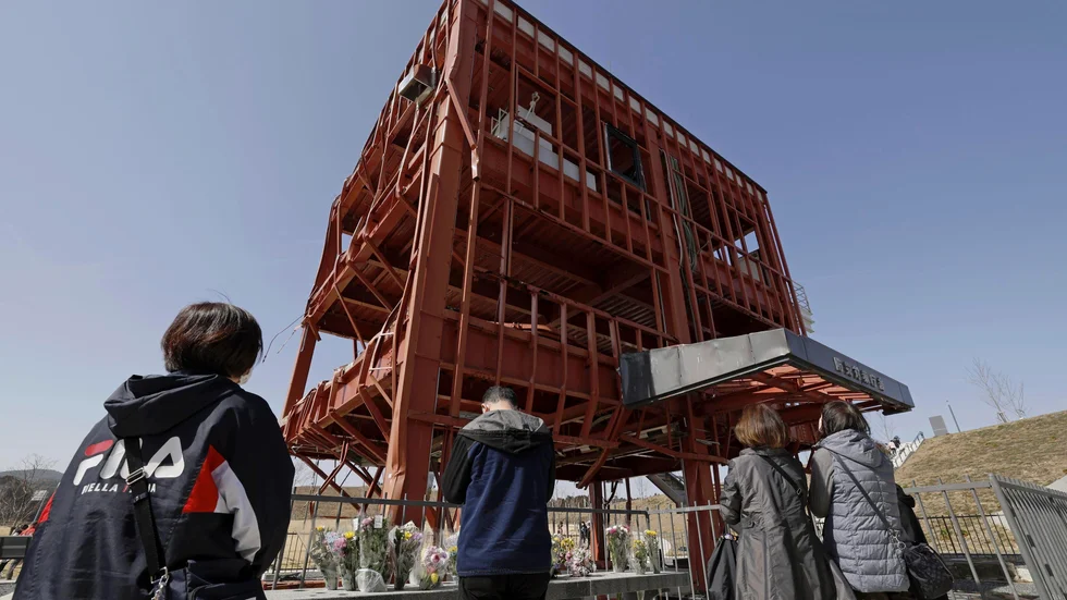 Anhöriga ber på årsdagen i Minamisanriku norr om Fukushima. Den söndertrasade byggnaden tillhörde räddningsverket, och många omkom där i tsunamin 2011.