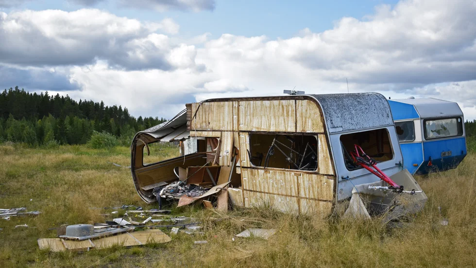 Husvagnens fasad har blivit totalt demolerad. Runt området är samtliga fordon vandaliserade.