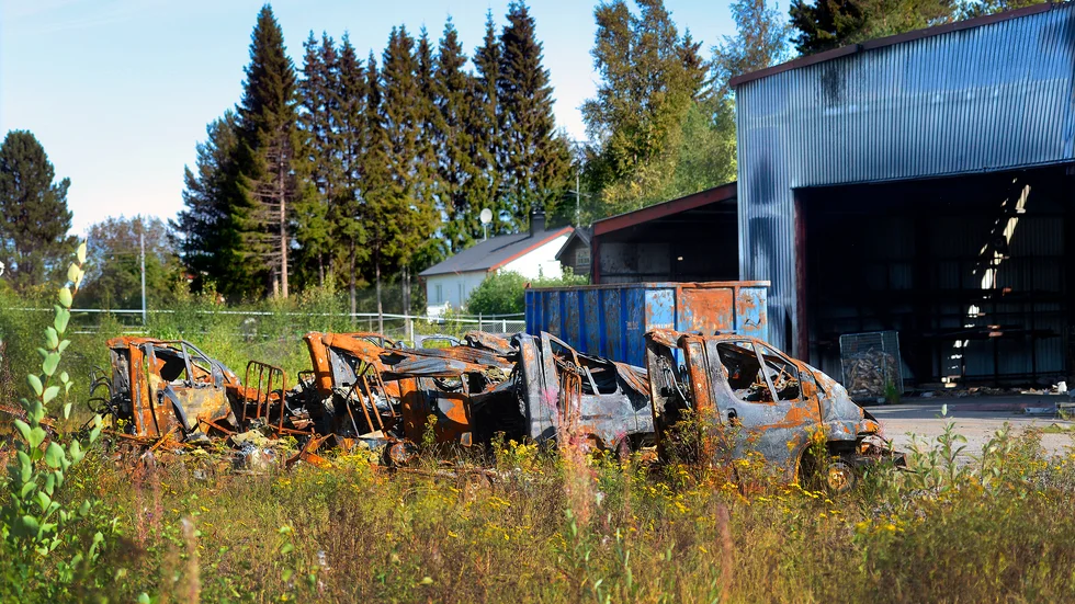Utanför den eldhärjade byggnaden står några utbrända fordon. 